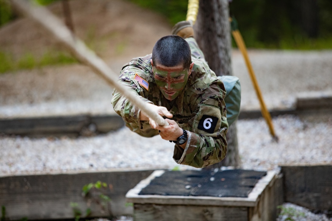 A soldier crawls along a rope above the ground.