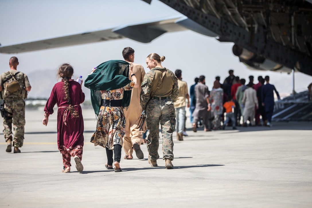 A Marine walks with children on a flightline.