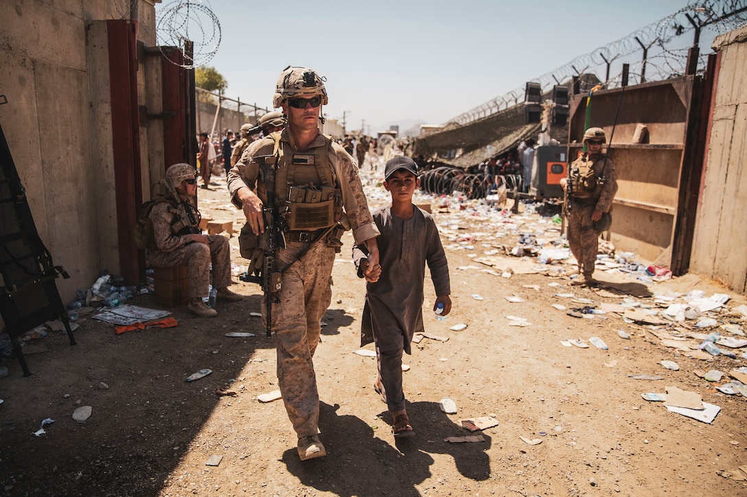 A Marine walks with a child and holds his hand in an area strewn with litter.
