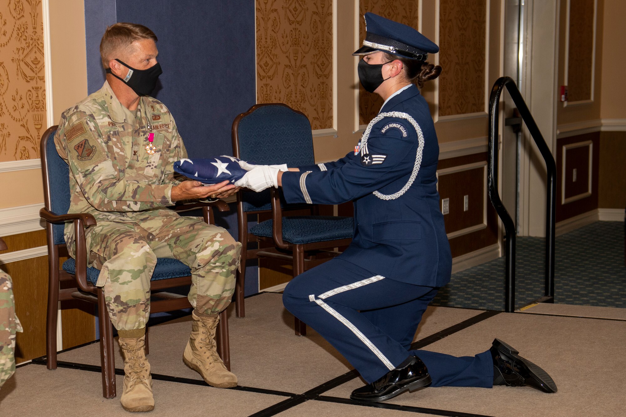 A member of the Honor Guard kneels before Col. Jason Price, outgoing 192nd Medical Group commander, and presents a folded U.S. flag to him upon his retirement.