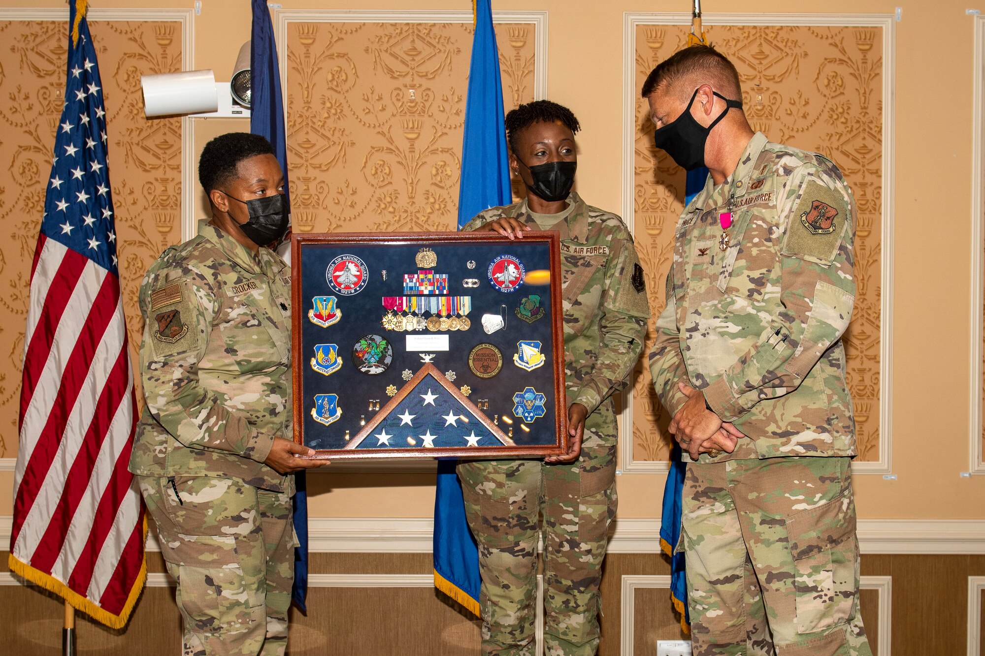 Two members of the 192nd Medical Group hold a shadow box as Col. Jason Price, outgoing MDG commander, looks at it.