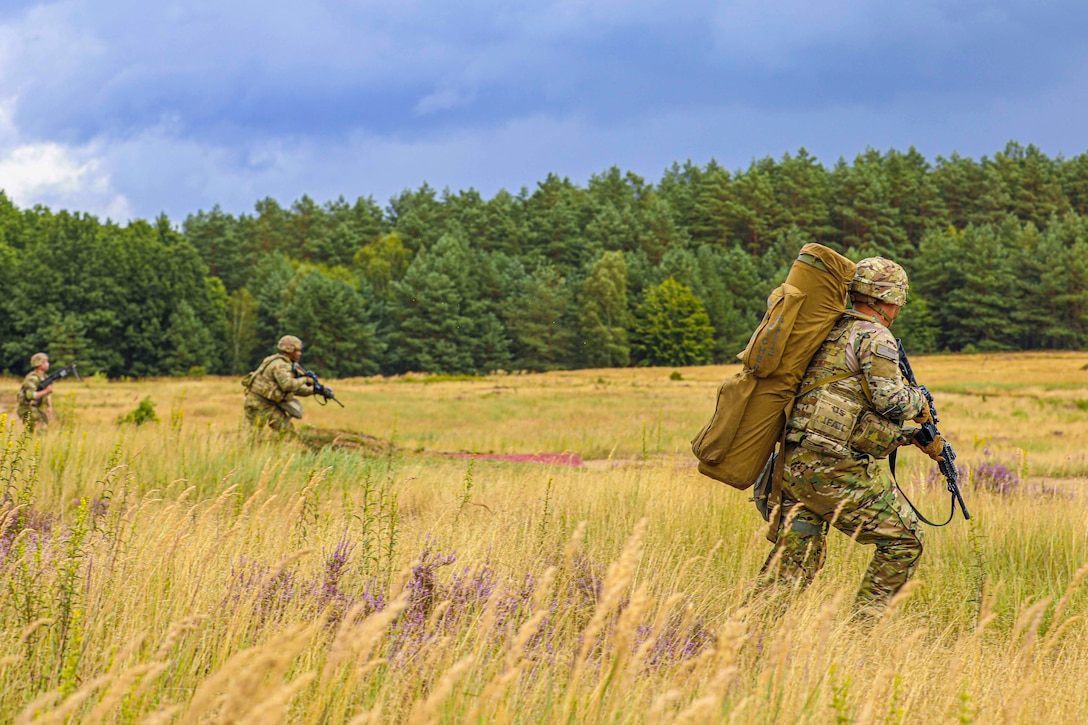 Three soldiers move through a grassy field with weapons drawn.