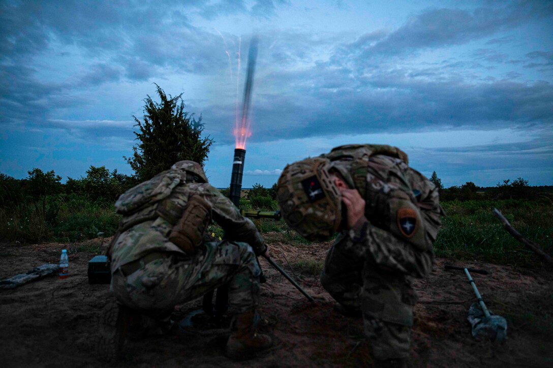 A soldier fires a mortar as another soldier covers their ears.