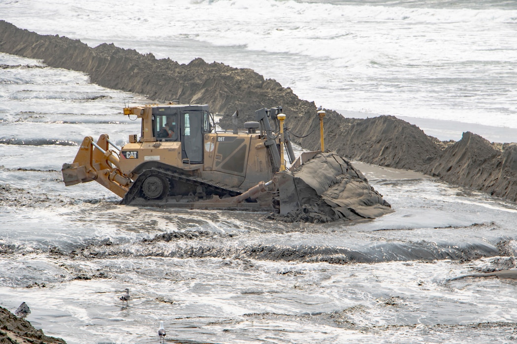 Beach front, ocean, sand being pumped ashore, construction equipment