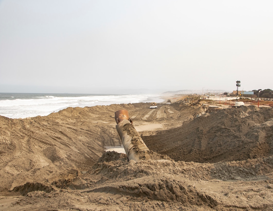 Beach front, ocean, sand being pumped ashore, construction equipment