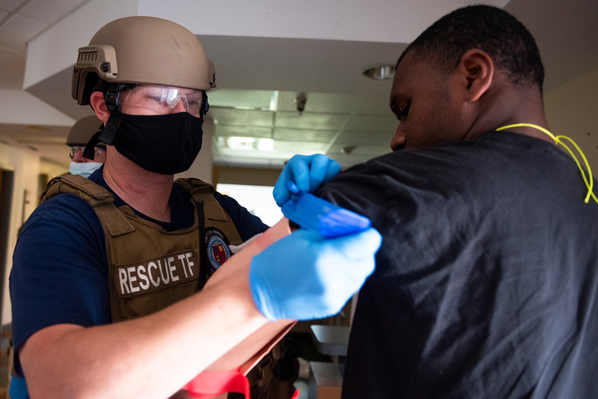 A paramedic from the 788th Civil Engineer Group Fire Department loosely places a tourniquet on the arm of a role-player with a simulated injury during an active shooter exercise, Aug. 18, 2021 at Wright-Patterson Air Force Base, Ohio. Readiness exercises are routinely held to streamline unit cohesion when responding to emergencies. (U.S. Air Force photo by Wesley Farnsworth)