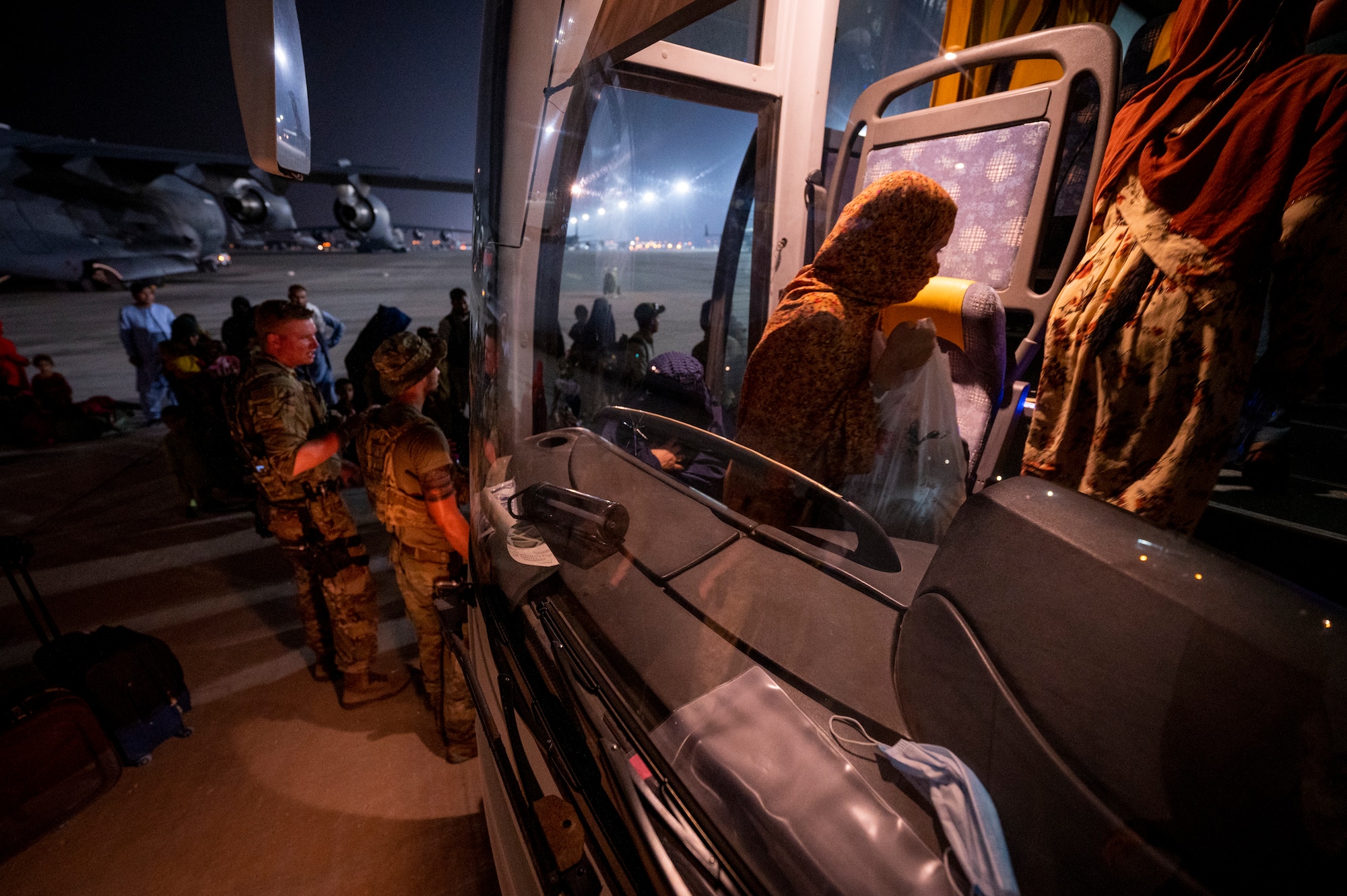 Airman assist Afghanistan evacuees onto a shuttle, Aug. 23, 2021, at Al Udeid Air Base, Qatar.