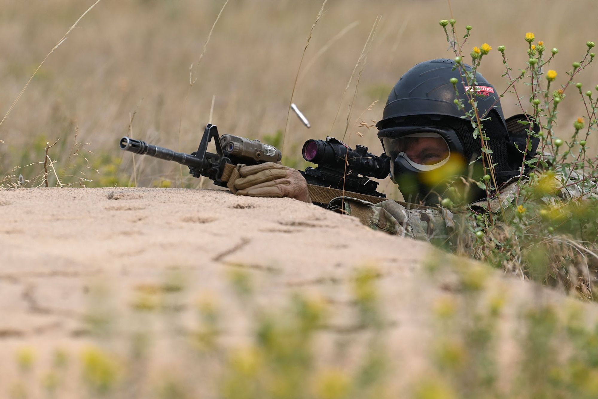 A defender from the 841st Missile Security Forces Squadron plays the role of an enemy combatant and fires simulated rounds with his M4 carbine during a training exercise Aug. 17, 2021, at the firing range on Fort Harrison, Mont. Simulated enemy combatants hid behind rocks, within tall grass and inside of buildings to test defenders’ lethality and teamwork in high-pressure situations. (U.S. Air Force photo by Airman Elijah Van Zandt)