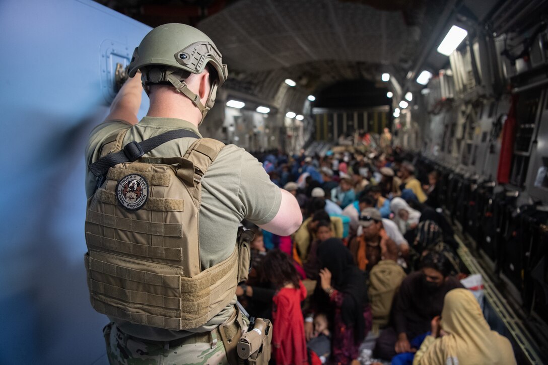 Hundreds of people sit on the floor inside a cargo aircraft. A lone U.S. service member watches over them.