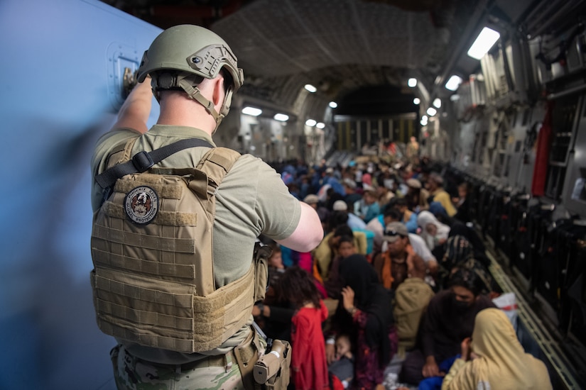 Hundreds of people sit on the floor inside a cargo aircraft. A lone U.S. service member watches over them.