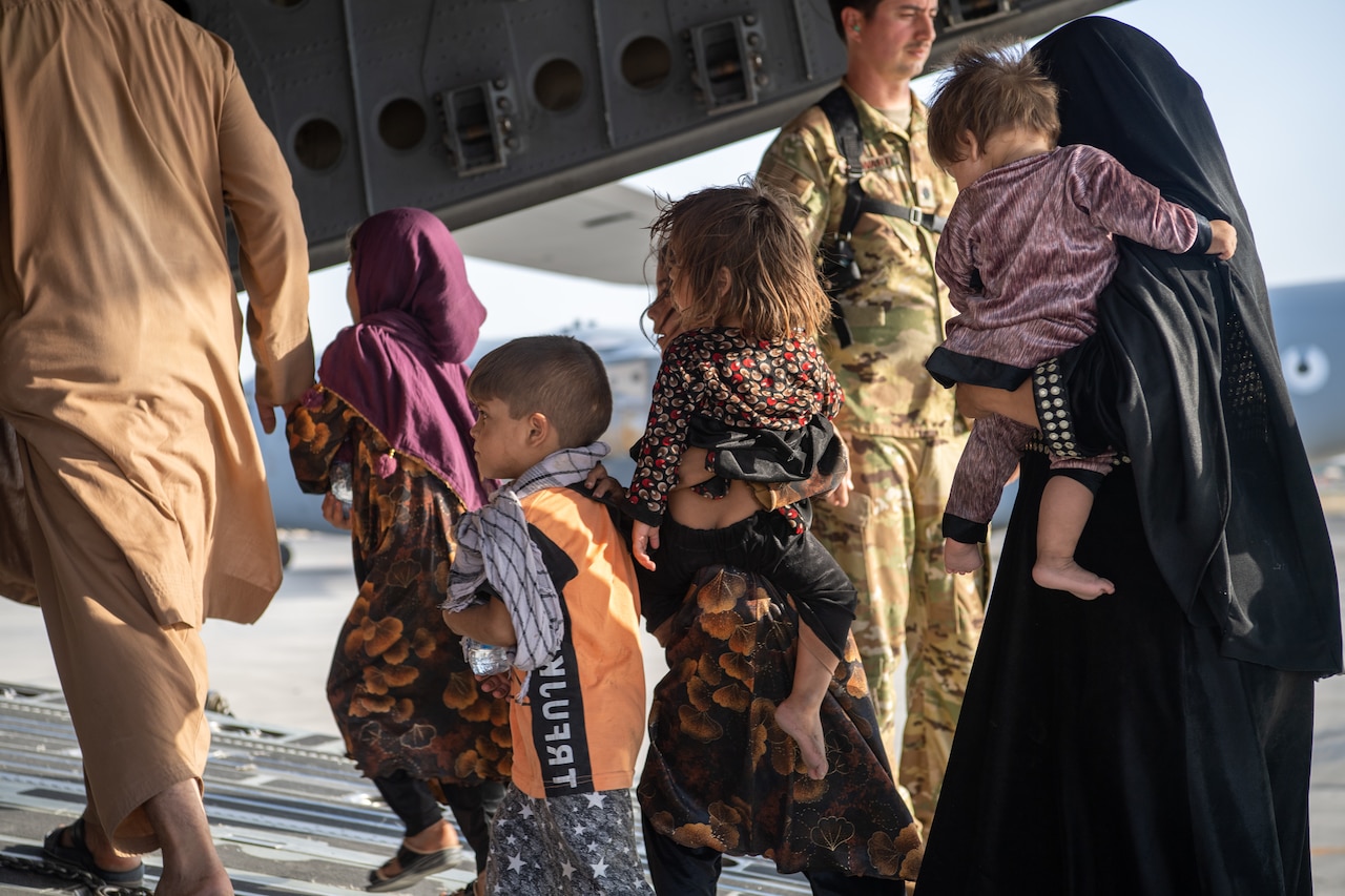 A woman and several children walk up the ramp of a military aircraft.