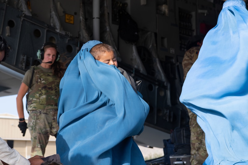 A robed woman carries a child up the ramp of a military aircraft.
