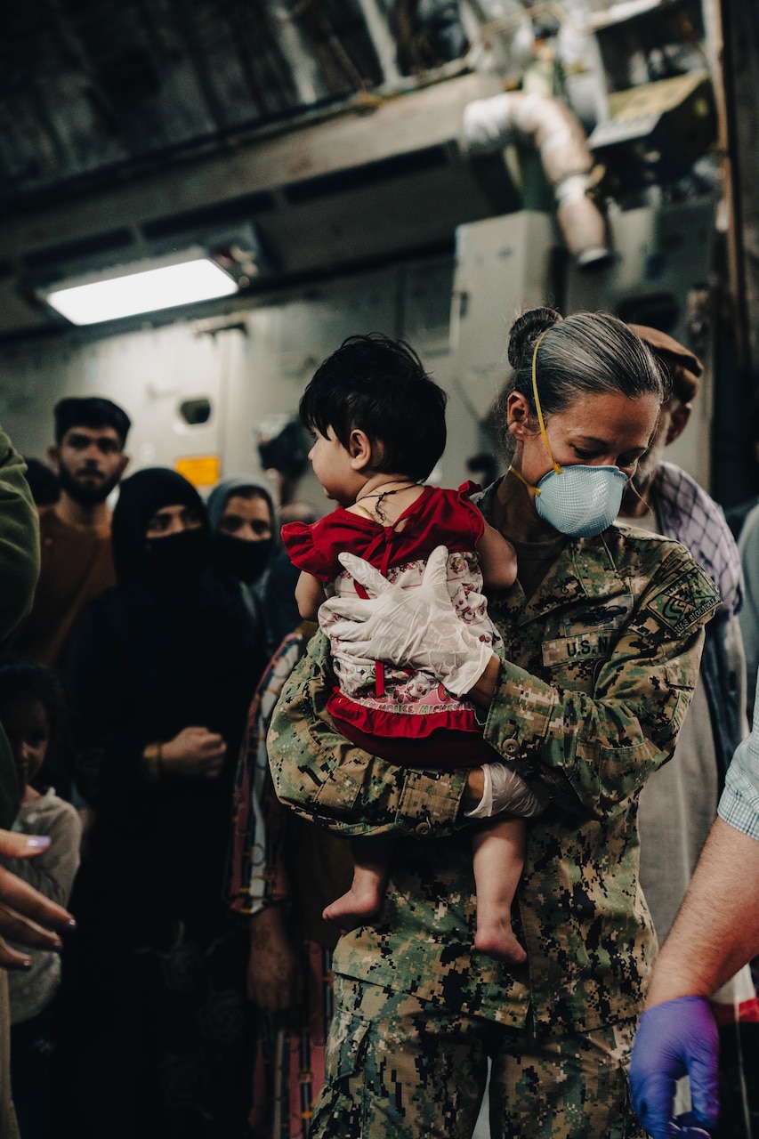 A woman in a military uniform carries a small child.