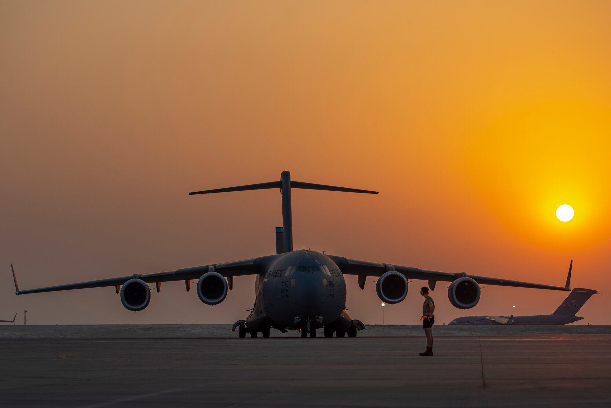 A member from the 379th Air Expeditionary Wing prepares to marshal a C-17 Globemaster lll as another C-17 taxis onto the flightline Aug. 23, 2021, at Al Udeid Air Base, Qatar.