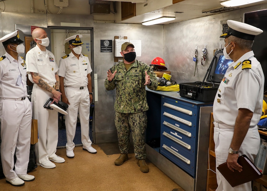 Navy Diver 1st Class John Thomason, assigned to the submarine tender USS Emory S. Land (AS 39), explains some of the capabilities of the dive locker to members of an Indian navy delegation during a tour of Emory S. Land as part of Malabar 2021.