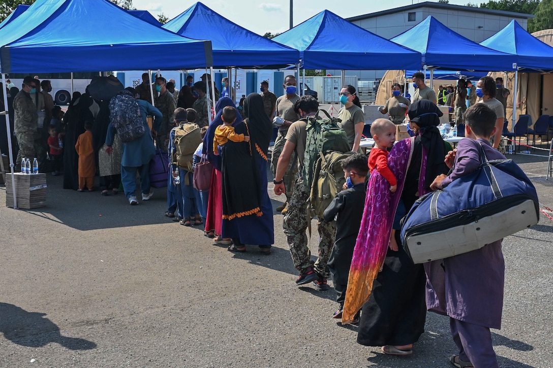 A group of people stand in line by blue tents.