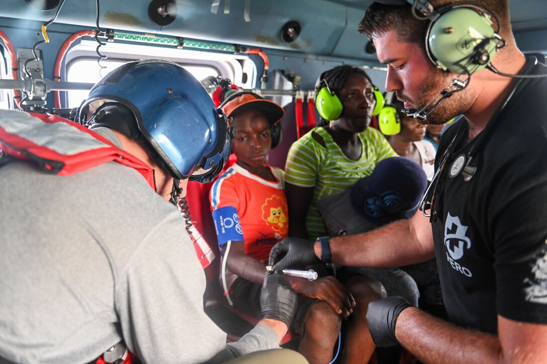 Personnel perform first aid on a patient on a helicopter.