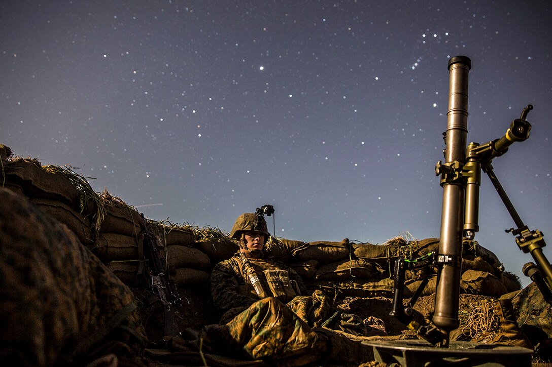 Marine takes cover in a fighting position next to a mortar.