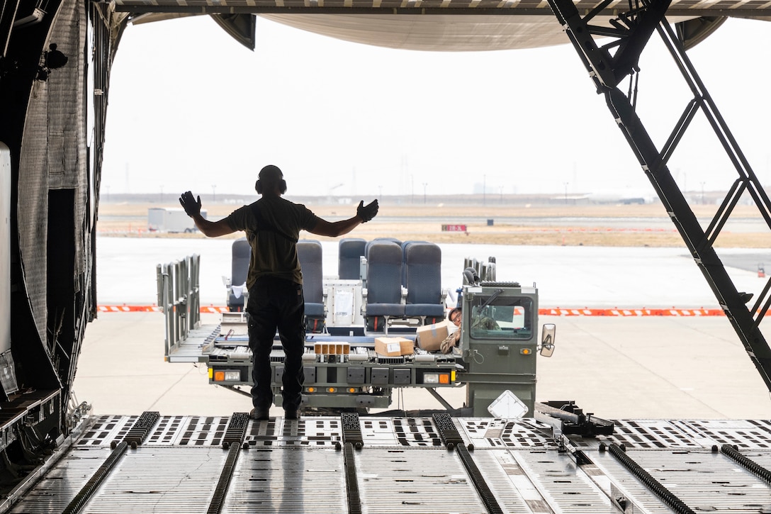 An airman stands with his arms in the air guiding a cargo loader.