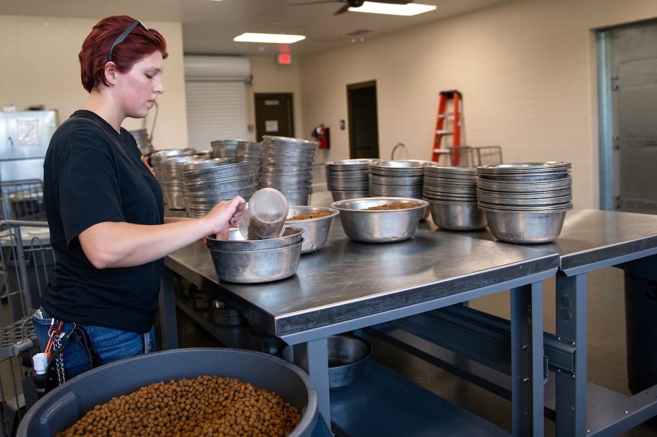 A woman pours dog kibble into large metal bowls.