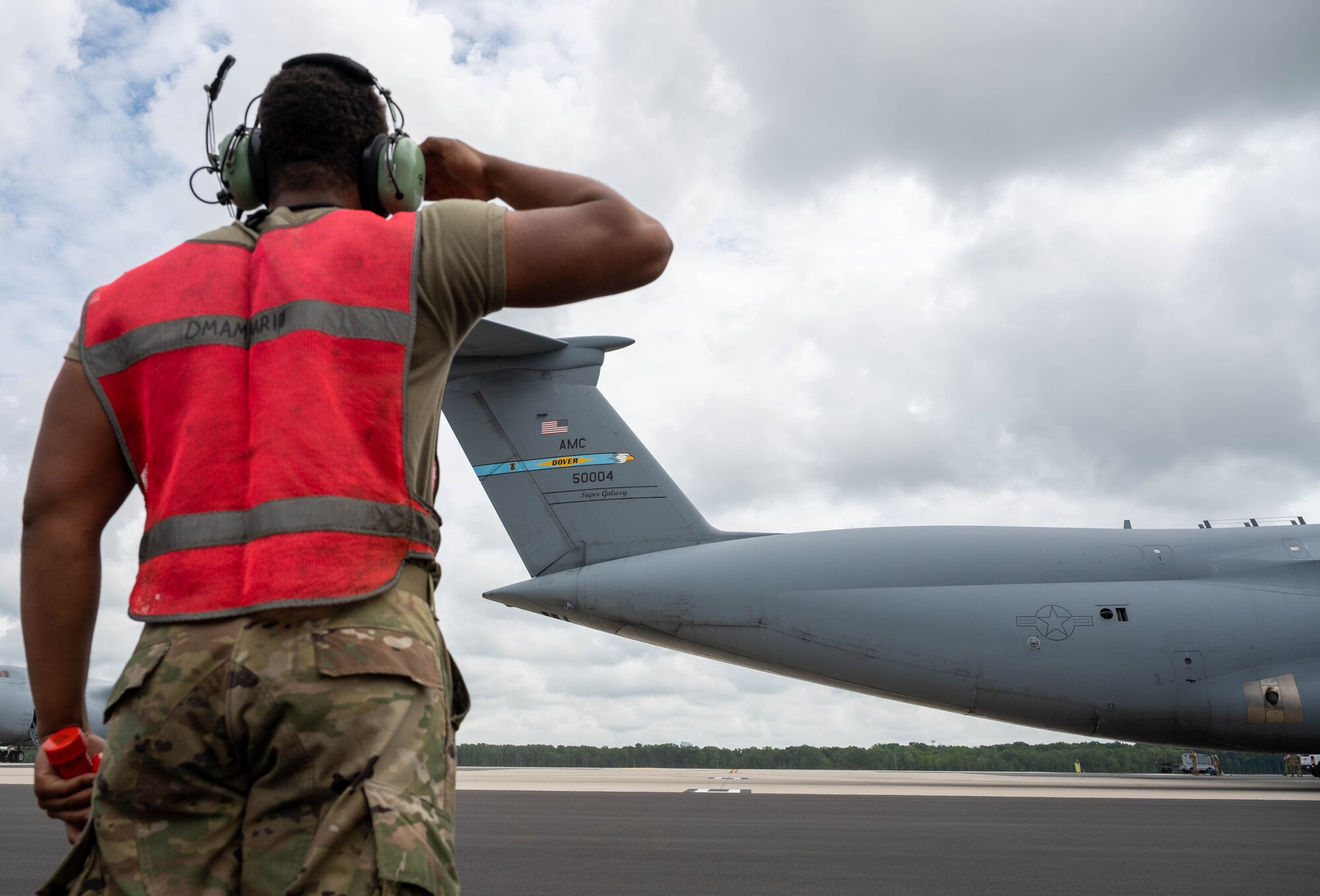 Senior Airman Deondre Douglas, 512th Maintenance Squadron, salutes a C-5M Super Galaxy as it taxis before taking off to Hamid Karzai International Airport, Afghanistan from Dover Air Force Base, Delaware, Aug. 16, 2021. Air Mobility Airmen play a key role in facilitating the safe departure and relocation of U.S. citizens, Special Immigration Visa recipients, and vulnerable Afghan populations from Afghanistan. (U.S. Air Force photo by Senior Airman Faith Schaefer)