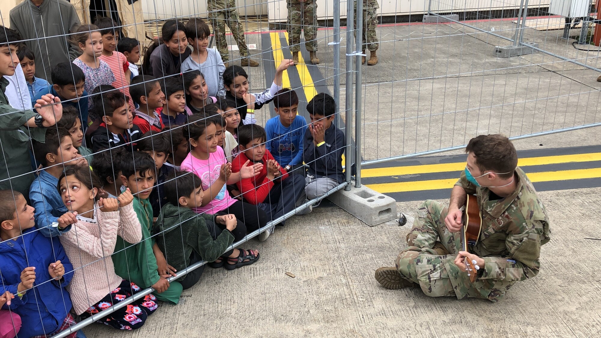 A U.S. Air Force Airman plays the ukulele for children from Afghanistan during Operation Allies Refuge at Ramstein Air Base, Germany, Aug. 24, 2021. Ramstein AB is providing safe, temporary lodging for evacuees. Many service members are also volunteering to raise morale for evacuees as they await transportation to more permanent resettlement locations.