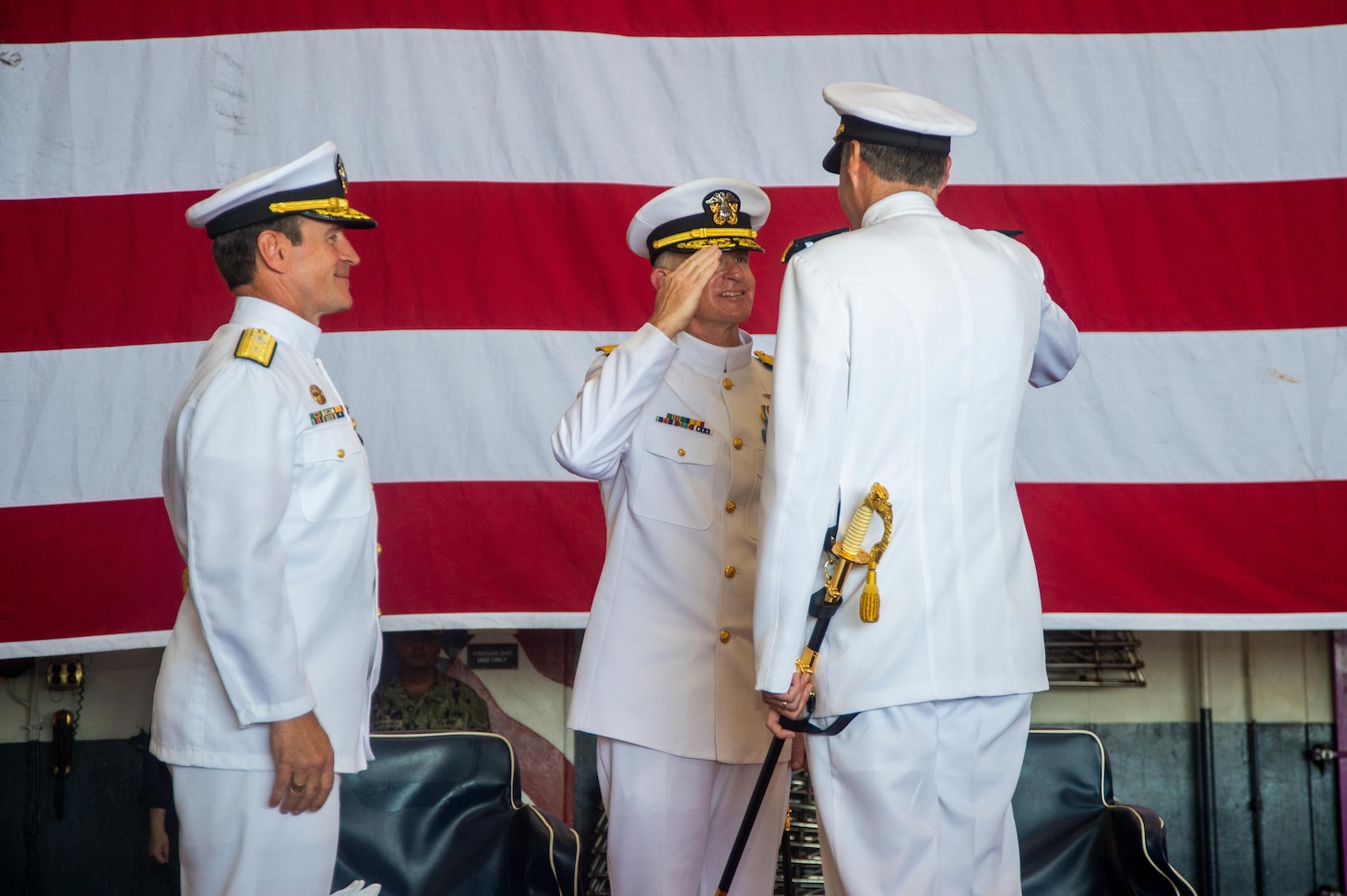 Rear Adm. Curt Renshaw, commander, Carrier Strike Group (CSG) 8, right, receives a salute from Vice Adm. Daniel Dwyer, commander, U.S. Second Fleet, middle, after relieving Rear Adm. Ryan Scholl, left, during a change of command ceremony for CSG-8 in the hangar bay of the Nimitz-class aircraft carrier USS Harry S. Truman (CVN 75).