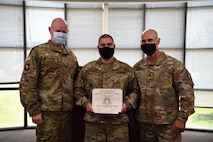 man in u.s. army uniform is presented with an award in front of a classroom.