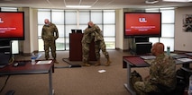 man in u.s. army uniform is presented with an award in front of a classroom.