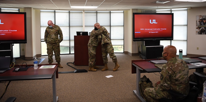 man in u.s. army uniform is presented with an award in front of a classroom.