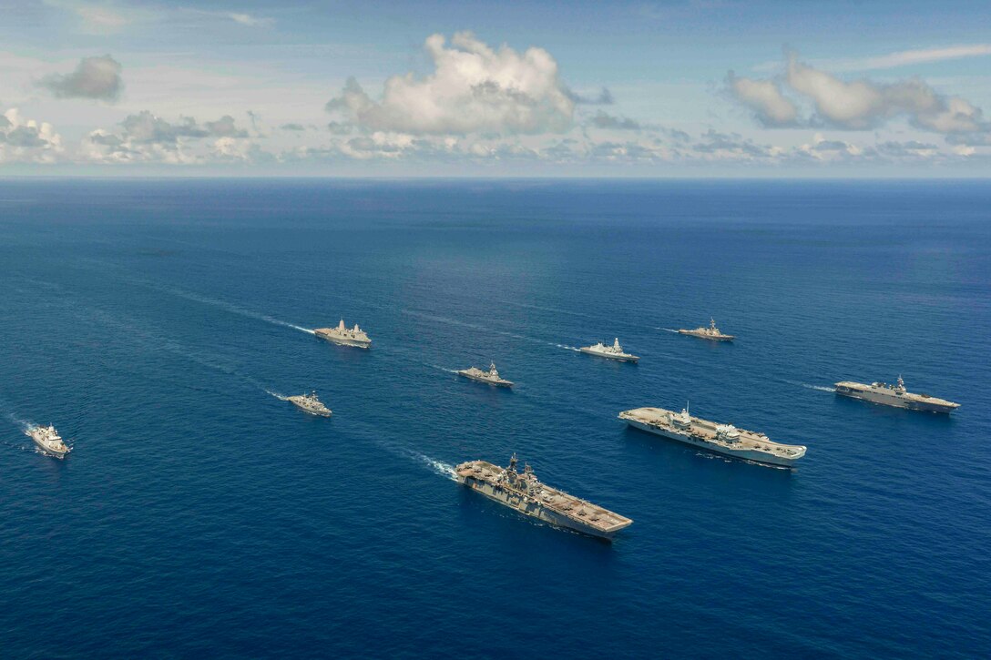Nine ships sail in formation through waters.