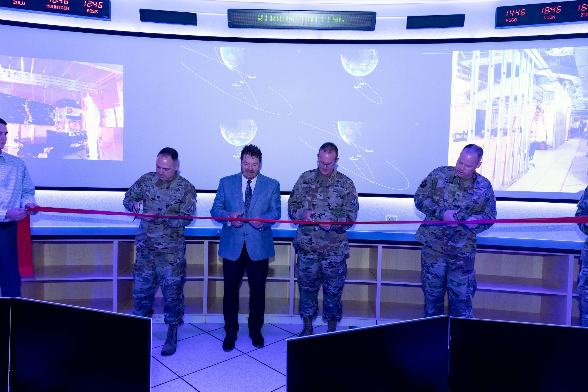 several men cutting a red ribbon inside a room with many tv monitors