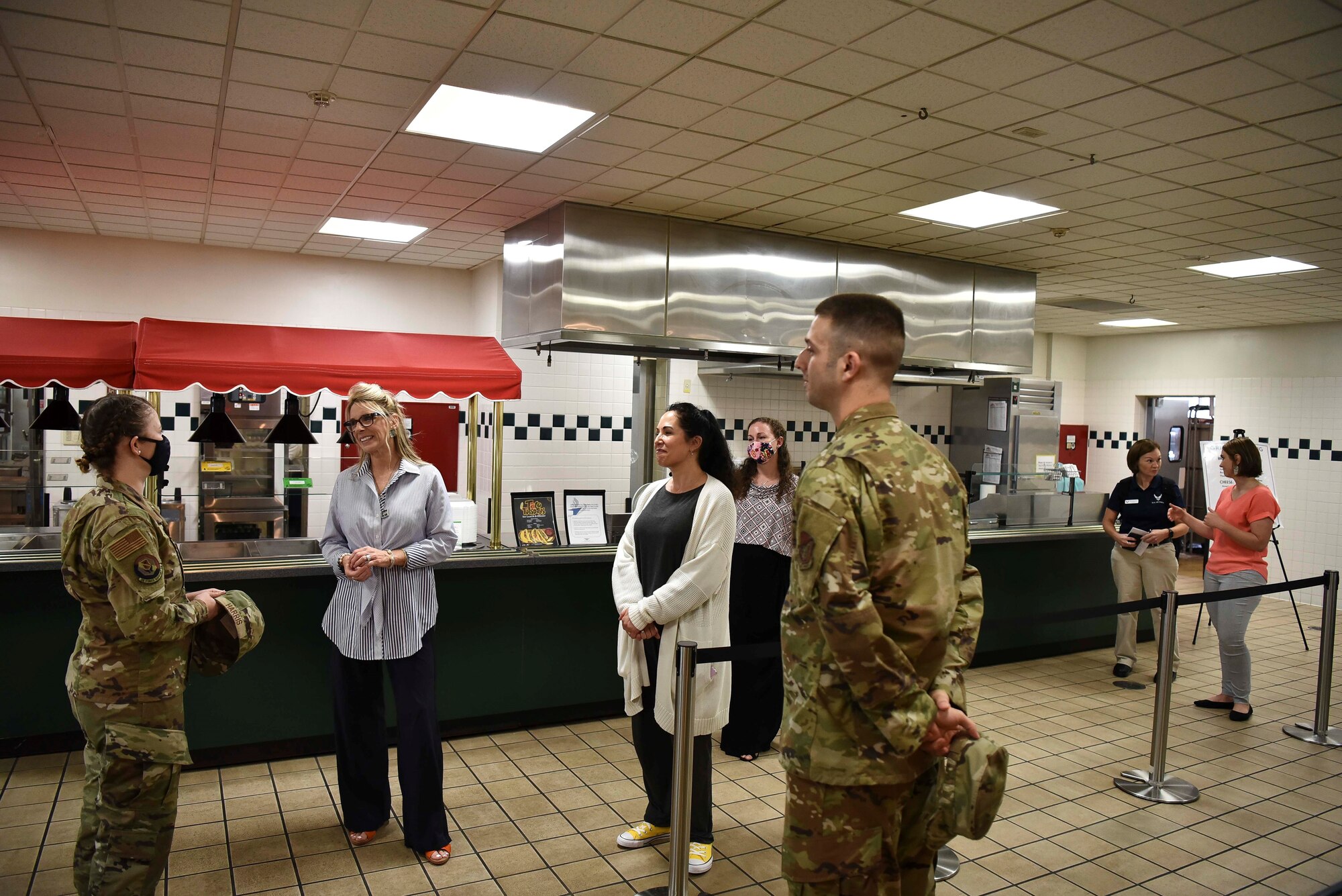 Two ladies listen to a military member in the Base's dining facility.