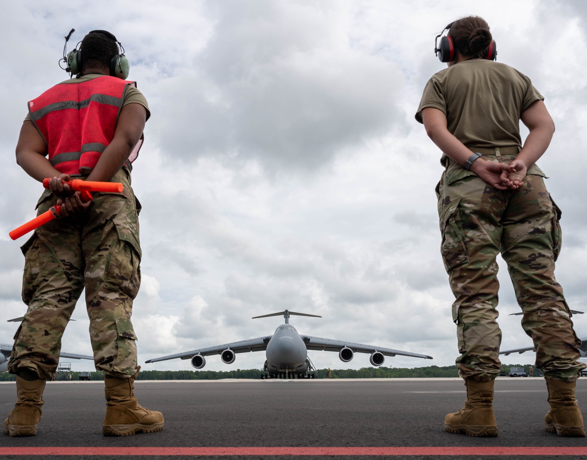 Senior Airmen Deondre Douglas and Janelle Ortwein, both 512th Maintenance Squadron crew chiefs, wait for a C-5M Super Galaxy to taxi before taking off to Hamid Karzai International Airport, Afghanistan from Dover Air Force Base, Delaware, Aug. 16, 2021. Air Mobility Airmen play a key role in facilitating the safe departure and relocation of U.S. citizens, Special Immigration Visa recipients, and vulnerable Afghan populations from Afghanistan. (U.S. Air Force photo by Senior Airman Faith Schaefer)