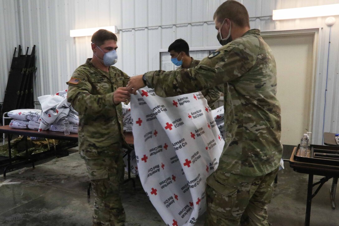 Soldiers fold blankets that say "Red Cross" on them.