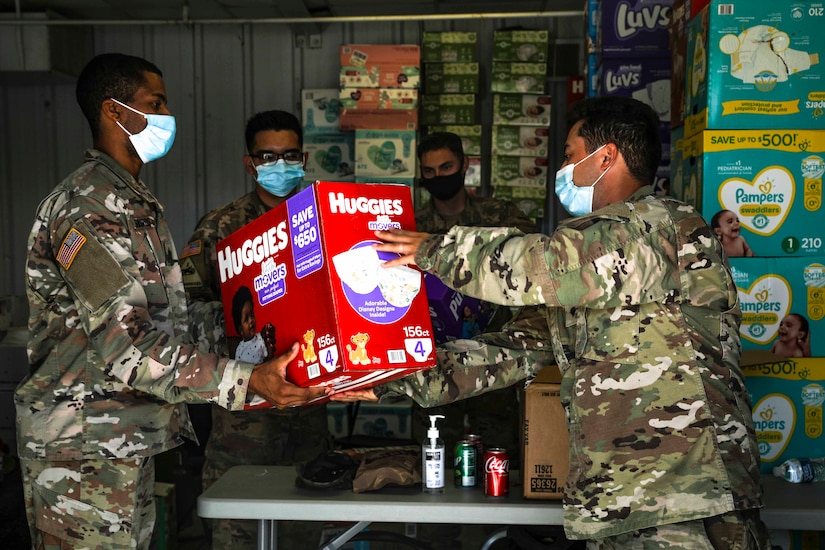 One soldier hands another soldier a box of diapers.