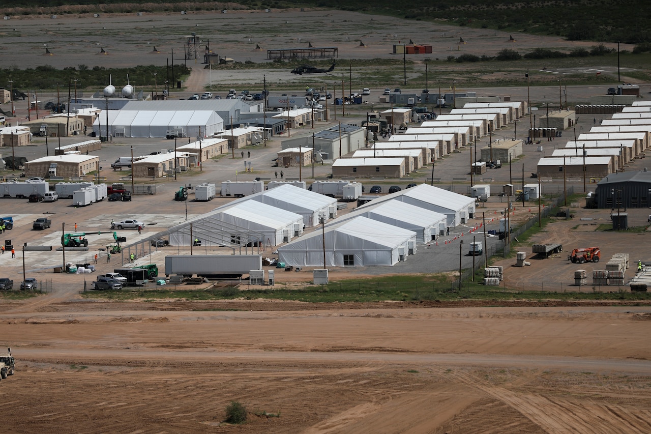 A grid of white temporary structures is spread out near an airfield.