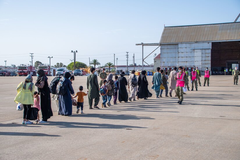 Civilians walk in a line across a flightline.