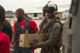 Team members with the U.S. Agency for International Development (USAID) pass a box of food to Hospital Corpsman 3rd Class Jace Borowiak to load onto an MH-60S Sea Hawk helicopter during a humanitarian aid mission