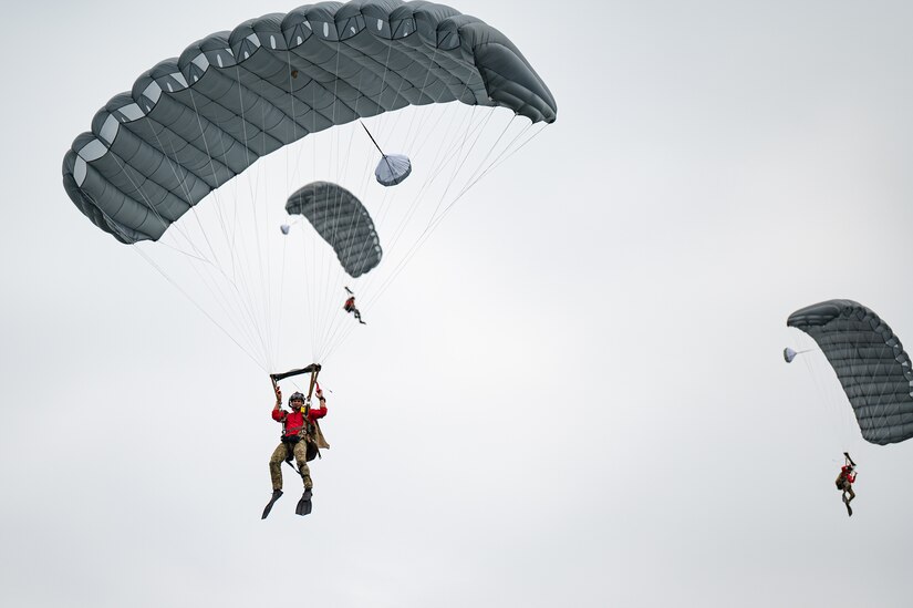 Airmen float through the sky wearing parachutes.