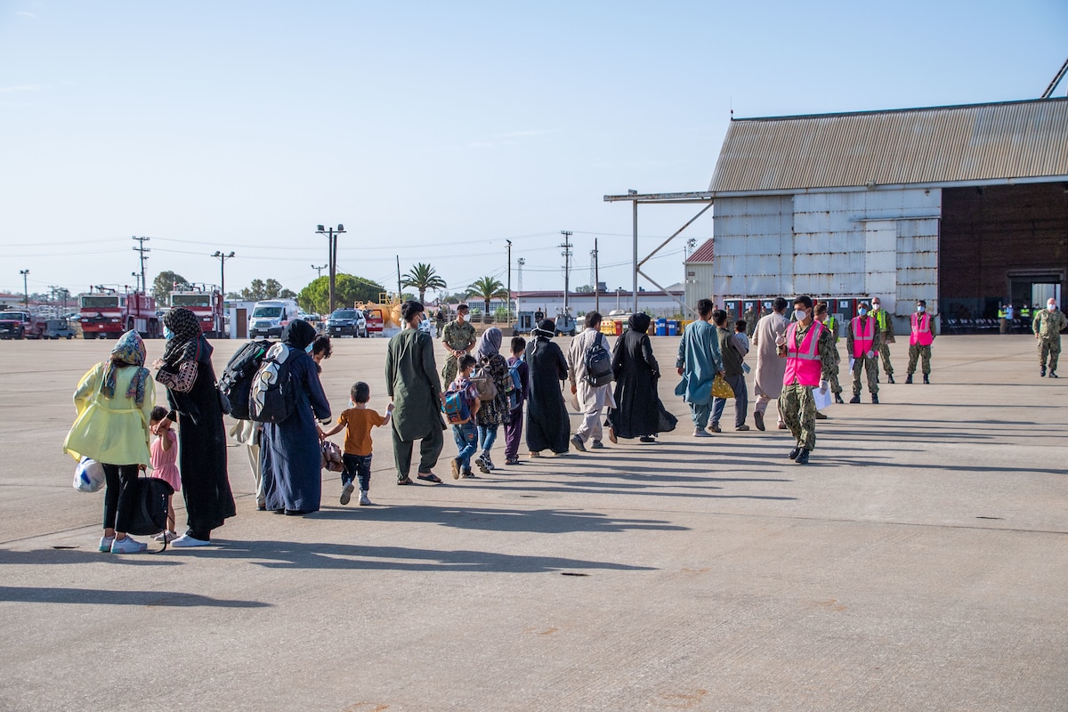 Civilians walk in a line across a flightline.