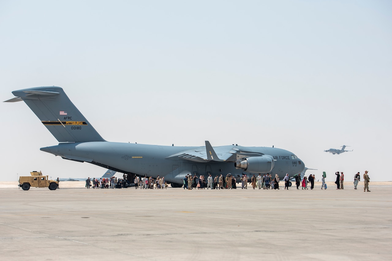 People exit the back of a large military aircraft.