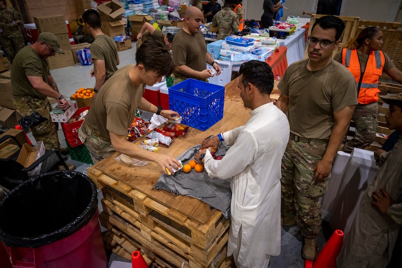 Individuals, most in uniforms, package food atop stacks of wooden pallets.