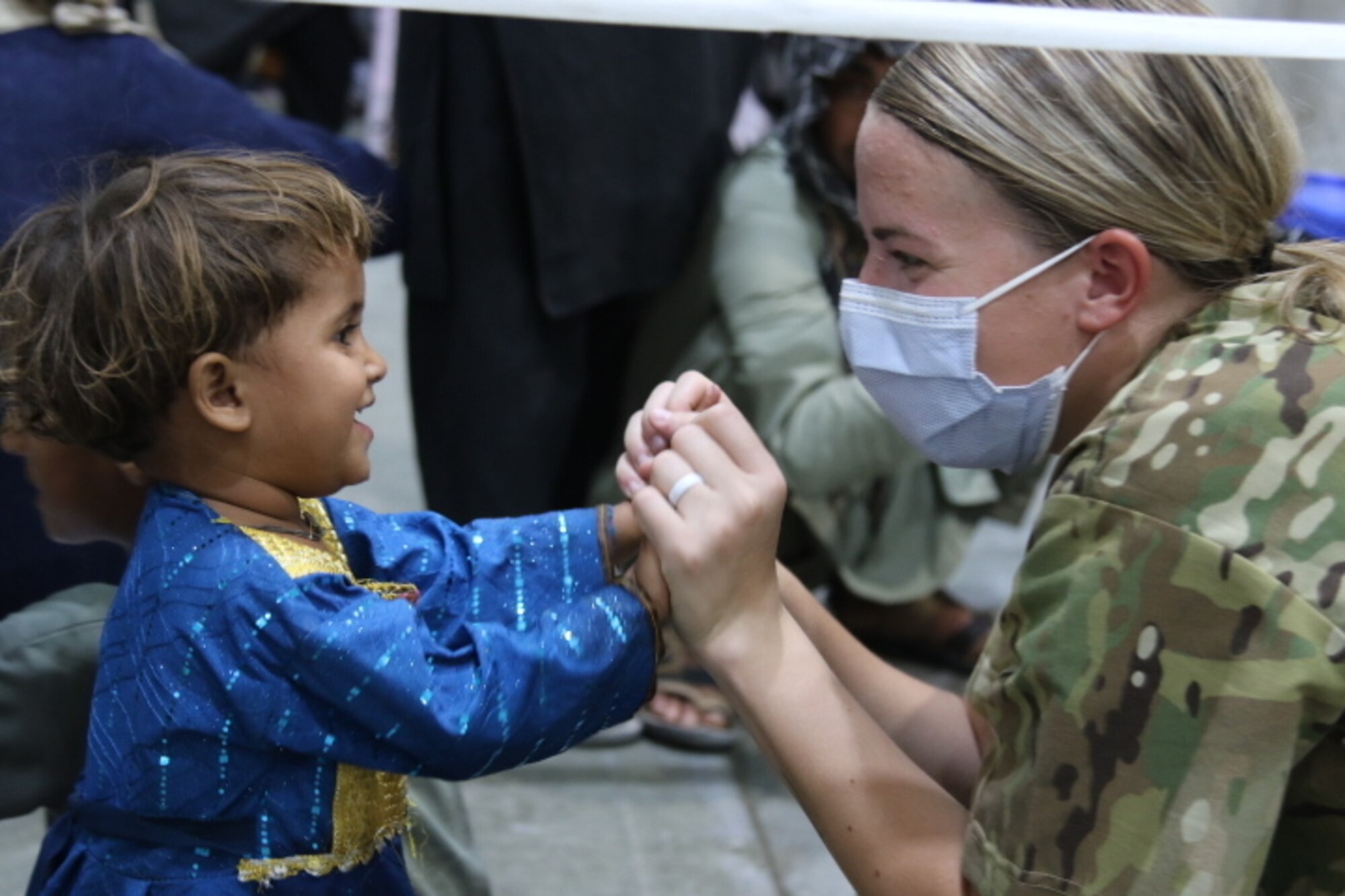A woman in a military uniform claps hands with a small child.