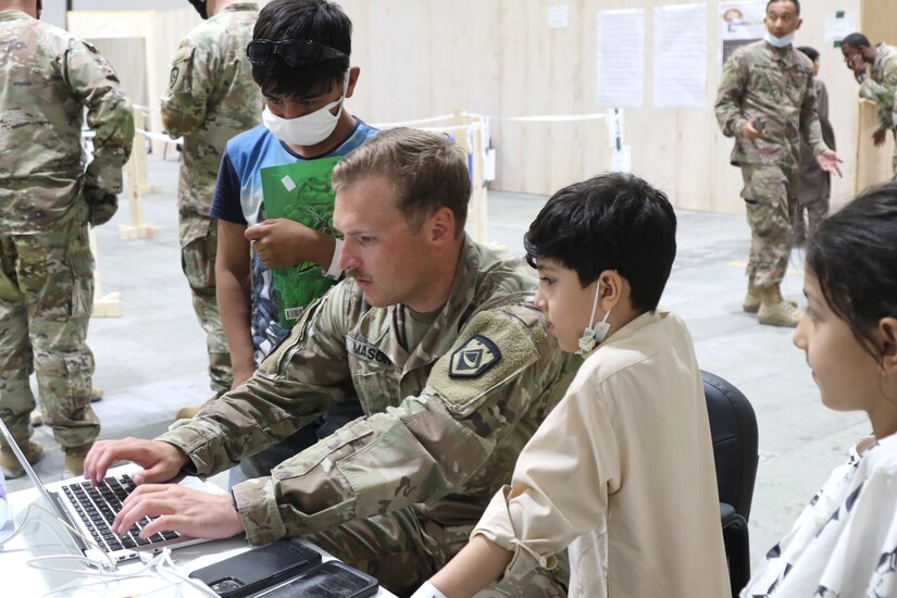 A U.S. Army National Guard Soldier with Task Force Spartan, U.S. Army Central shares his computer to entertain Afghan evacuee children at Camp Buehring, Kuwait, Aug. 25, 2021. USARCENT Soldiers hit it off quickly with the children at the facility, finding ways to bring smiles and entertain them through the arrival process. (U.S. Army photo by Pfc. Katelynn Bissell)