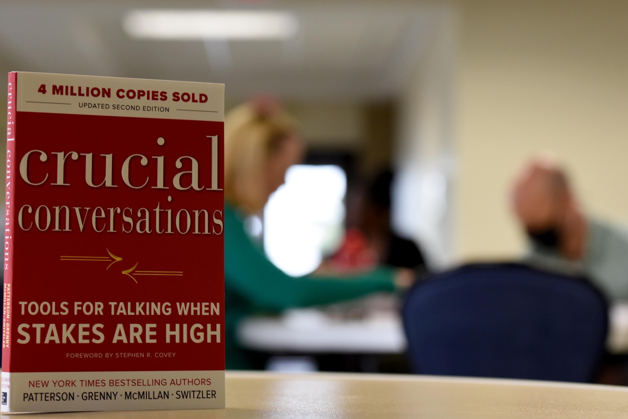 Book stands on table with people in the background.