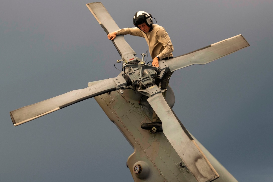 A sailor works on the rotor of a helicopter.