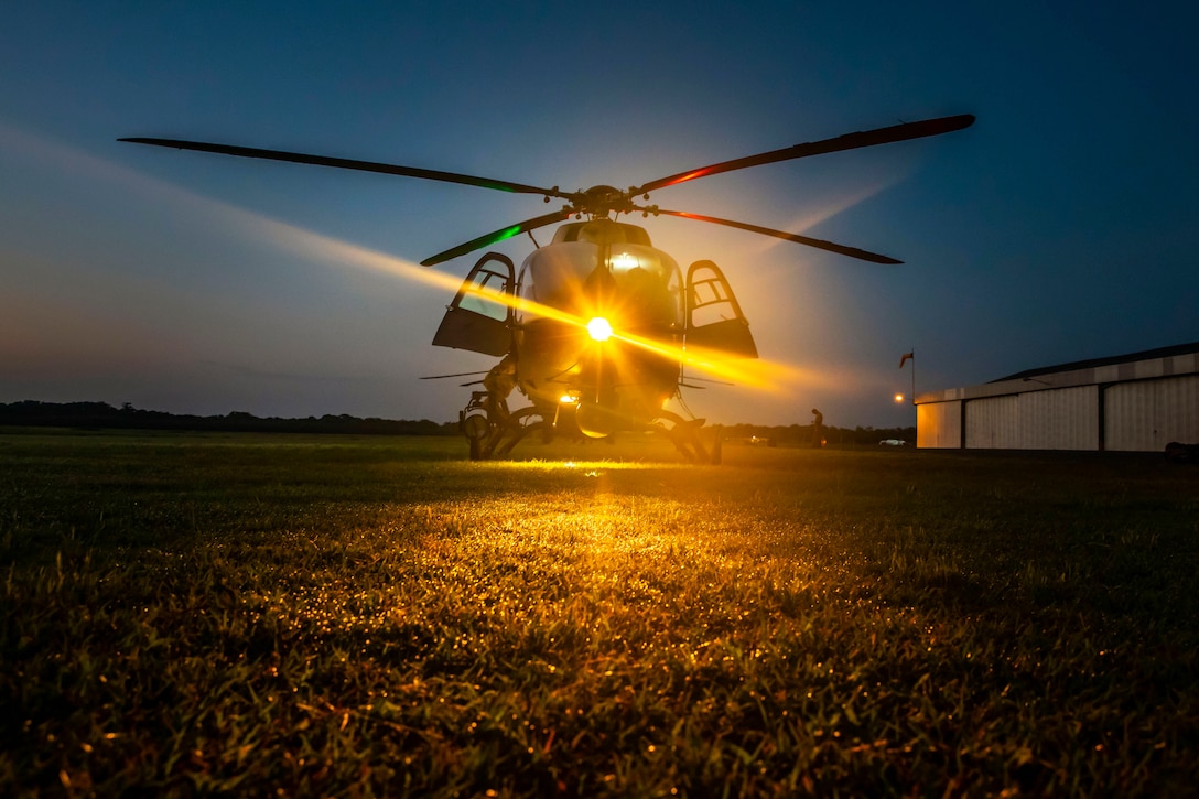 A helicopter sits in a field illuminated by red and green lights.