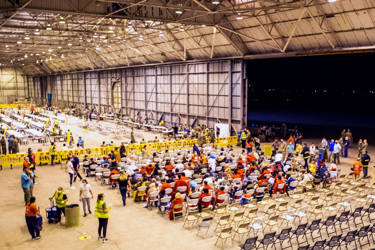 People file into a large room and take seats as seen from a high angle.