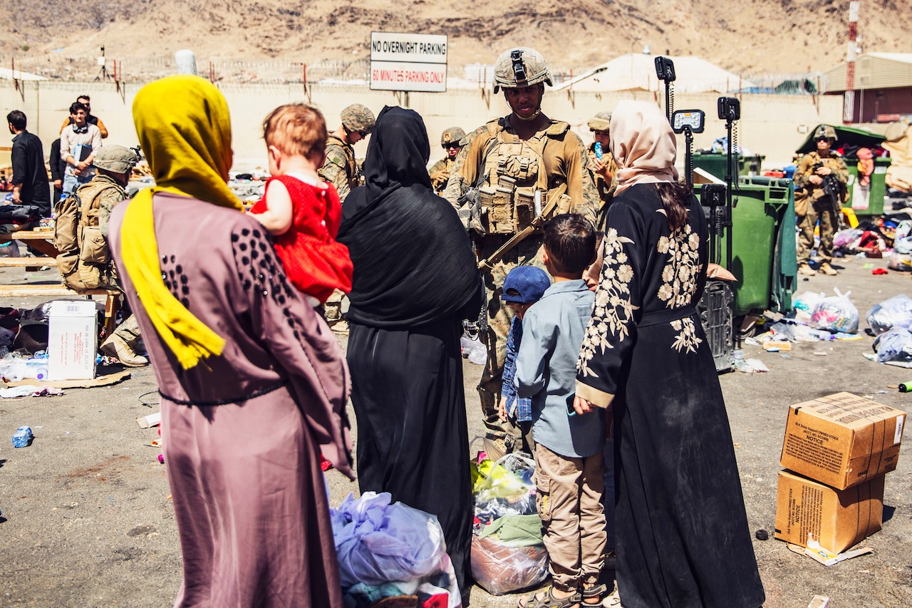 A Marine faces a group of civilians with others in the background.